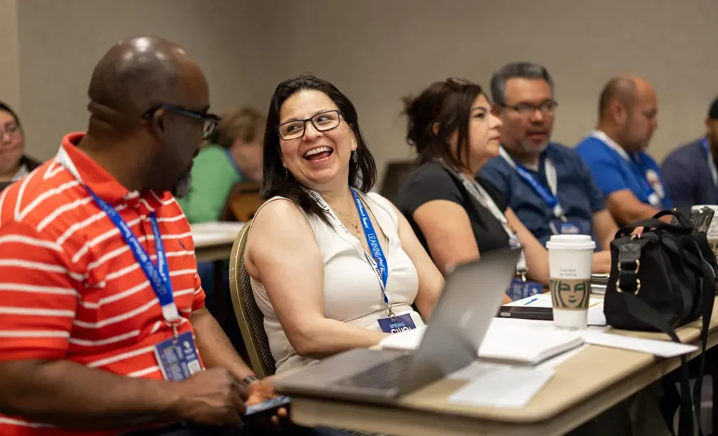 Educators smile and engage in conversation during a Spring CUE breakout session, seated with laptops and conference materials in an interactive learning environment.