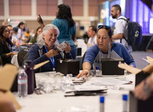Educators participate in a hands-on activity during a Spring CUE session, smiling and collaborating at a table filled with materials and conference supplies.