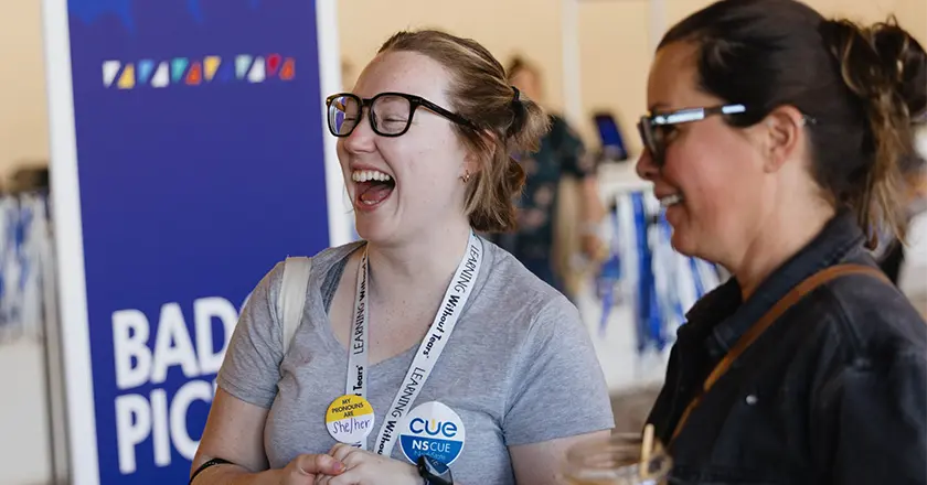 Two attendees laugh together near the badge pickup area at the Spring CUE Conference, capturing the excitement of the event’s opening moments.