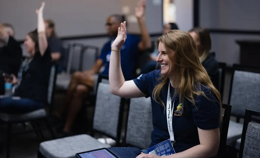 Smiling educator raises her hand to participate during a professional learning session at a conference.